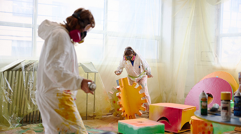 Deux artistes habillées en blanc peignent des objets de différentes formes avec des canettes de peinture